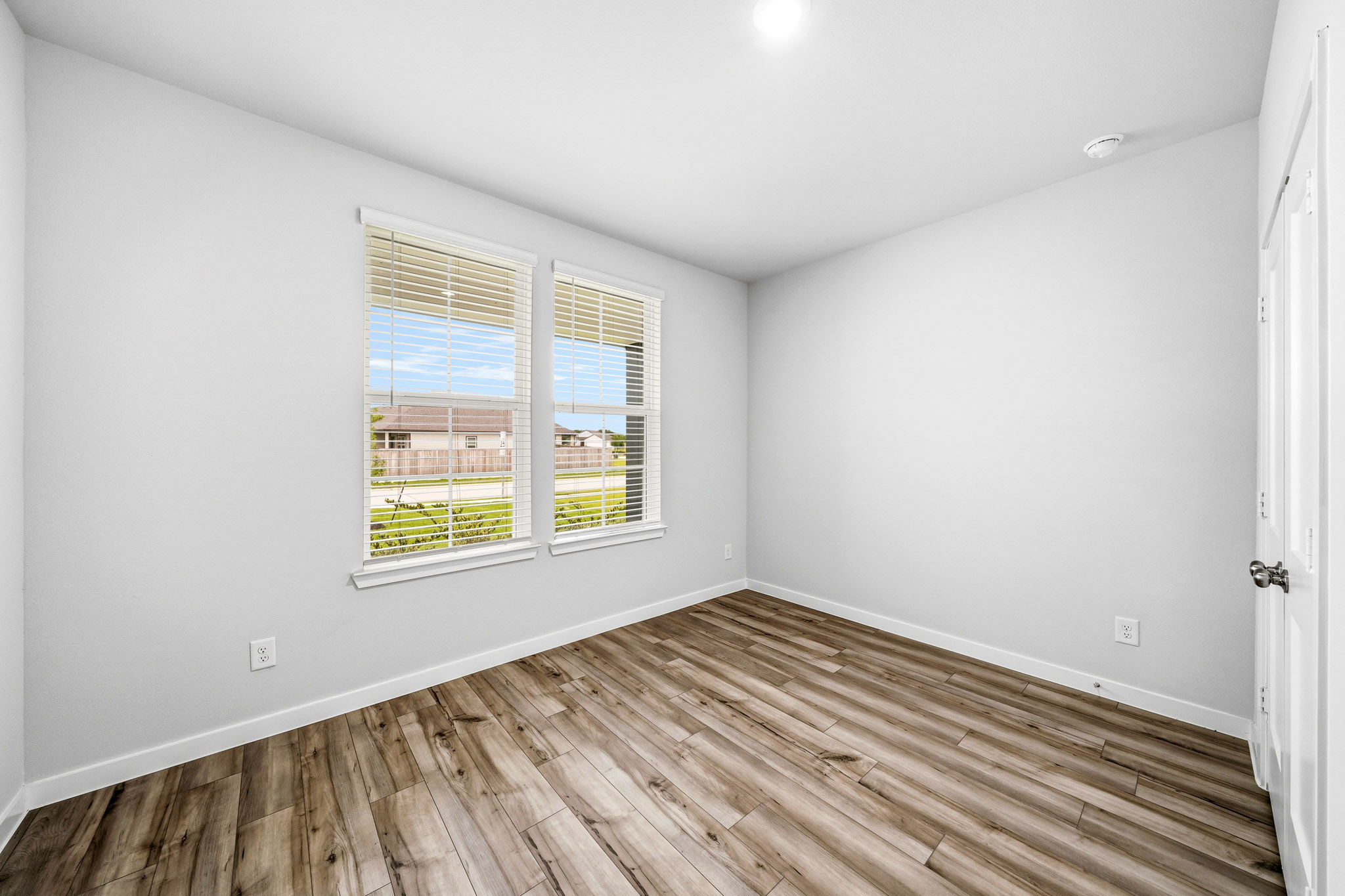 A room with a wood floor and a window with blinds.